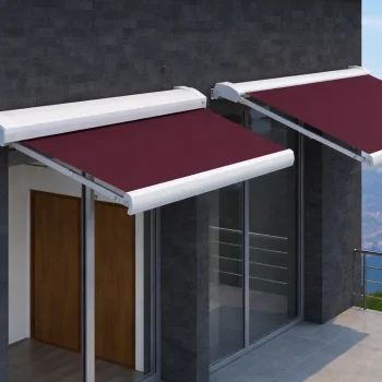 Toldo de braços articulados compacto instalado numa fachada, com estrutura branca e lona vermelha, a proteger a zona de janela e varanda.