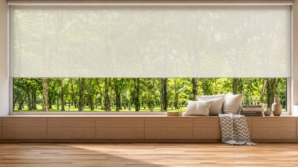 Estores de rolo de grandes dimensões instalados numa sala com grande janela envidraçada